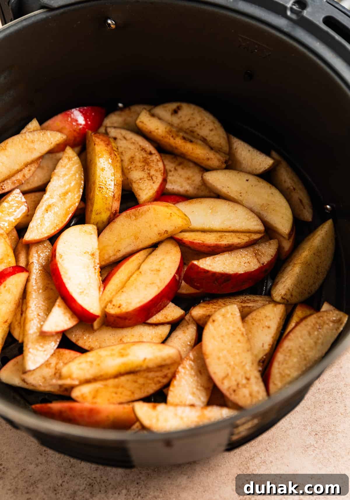 Air fryer basket with sliced apples tossed in oil and cinnamon before cooking.