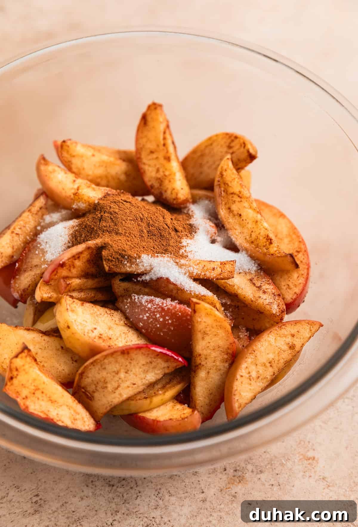 Air fryer cinnamon apples in glass mixing bowl with melted butter, sugar and cinnamon poured on top.