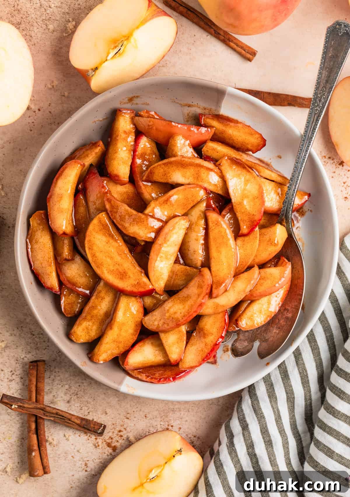 Serving plate with buttery cinnamon fried apples with serving spoon and cinnamon sticks beside dish.
