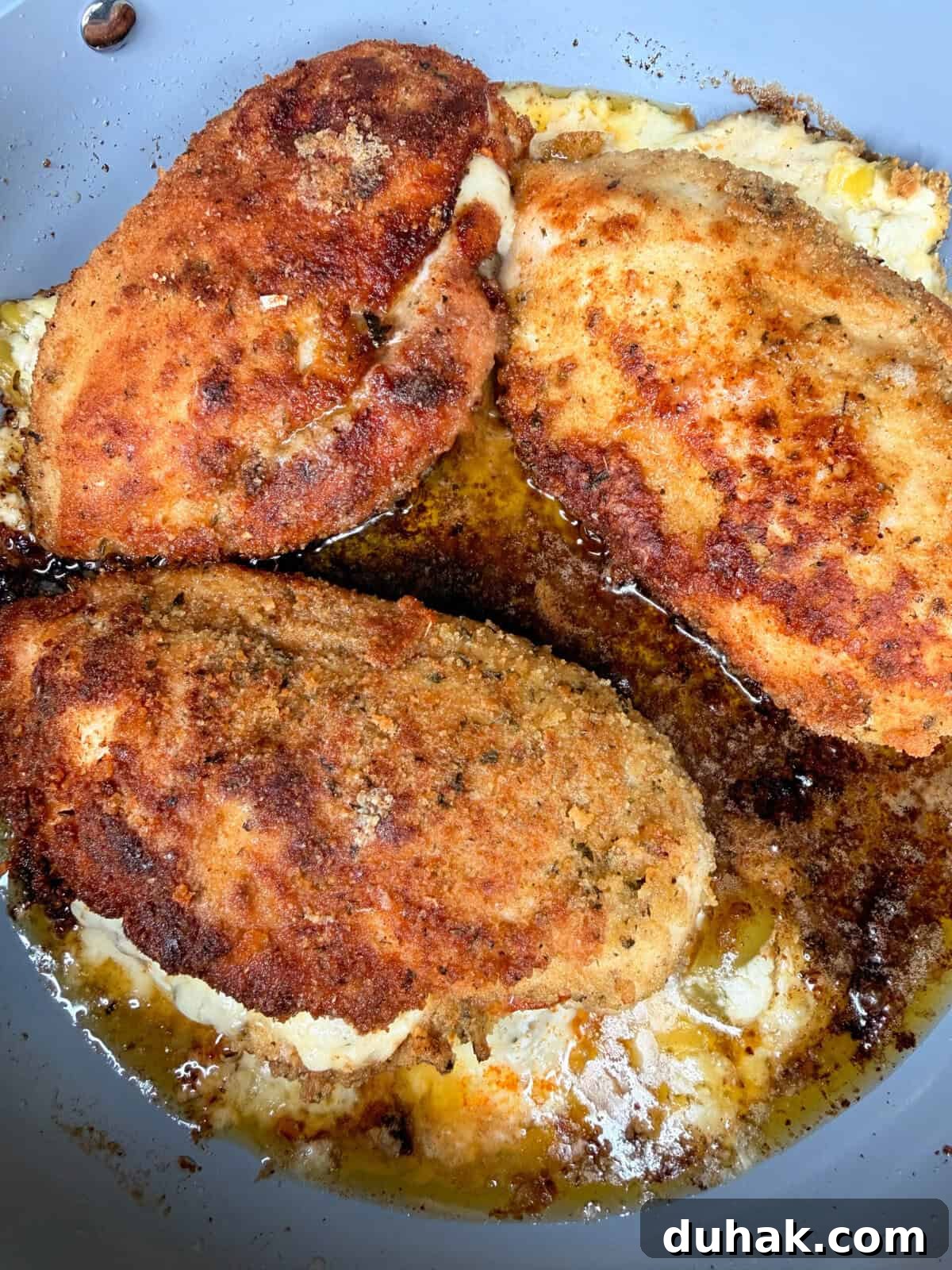 Creamy Spinach & Cheese Stuffed Chicken Cutlets Recipe 8 Three breaded and pan-fried chicken breasts are cooking in a skillet with sizzling oil and melted butter, creating a golden brown and crispy crust.