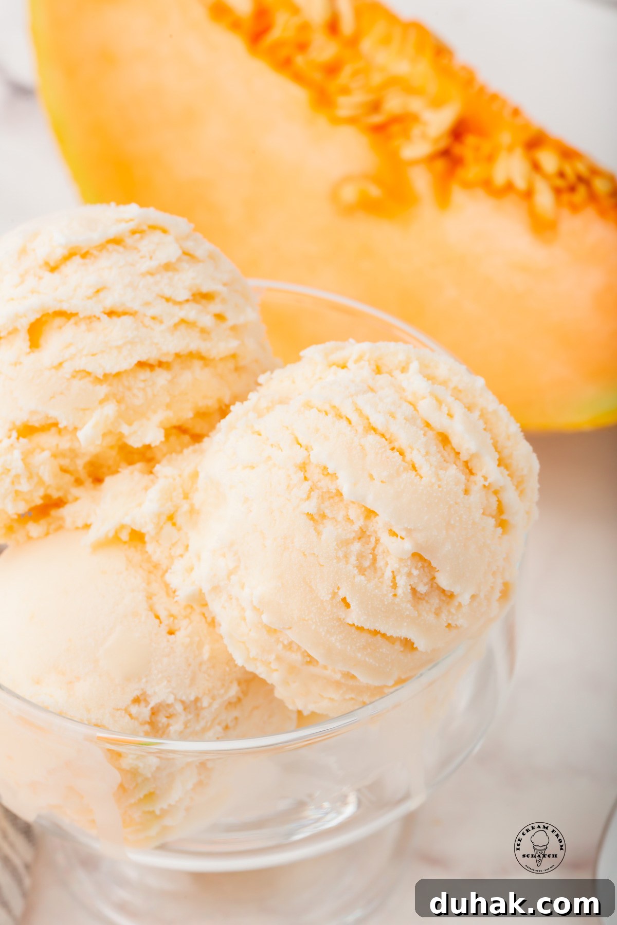 Creamy Cantaloupe Ice Cream Recipe: Refreshing Summer Treat 5 A glass dish filled with scoops of melon ice cream. A large wedge of cantaloupe is in the background.