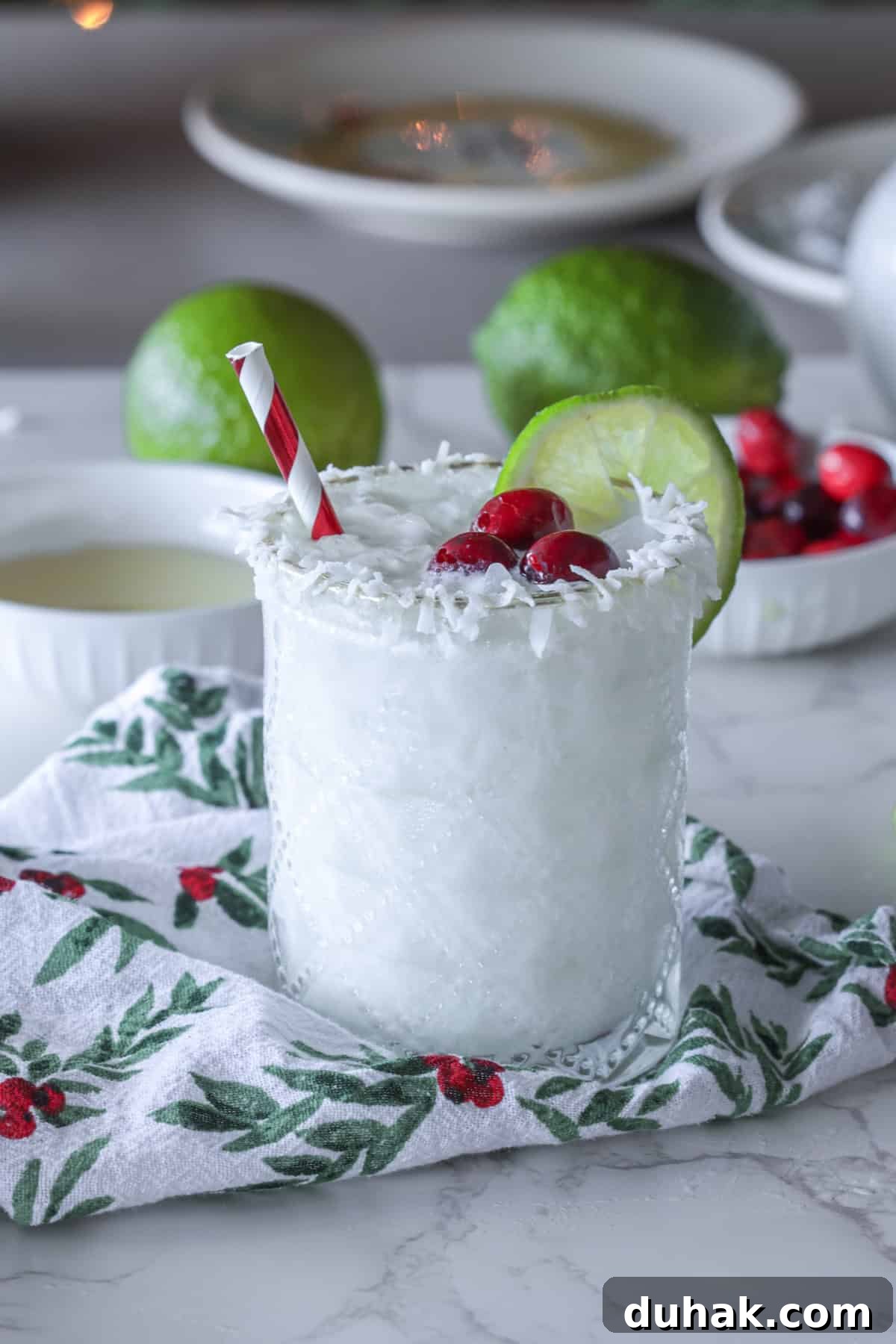 White margarita with straw in a glass with coconut flakes garnished with cranberry and lime.