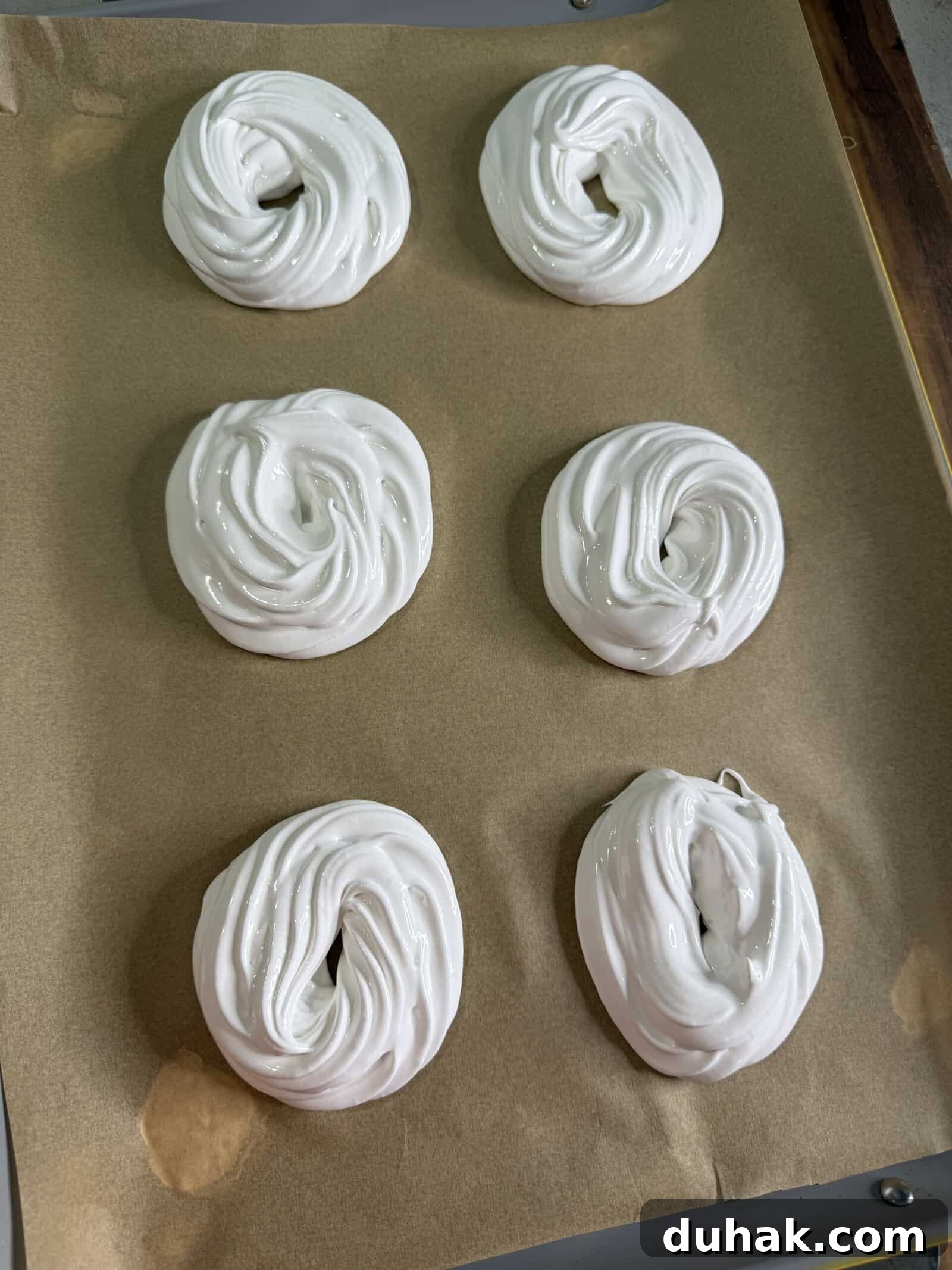 Yuzu Curd Pavlova Recipe: Light Citrus Meringue Cake 4 Six swirled mounds of white meringue are arranged in two rows on a parchment-lined baking sheet, ready to be baked.