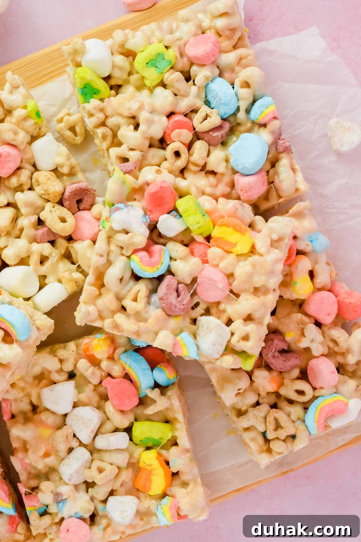 stacked lucky charm rice krispie treats cut into squares on white parchment.