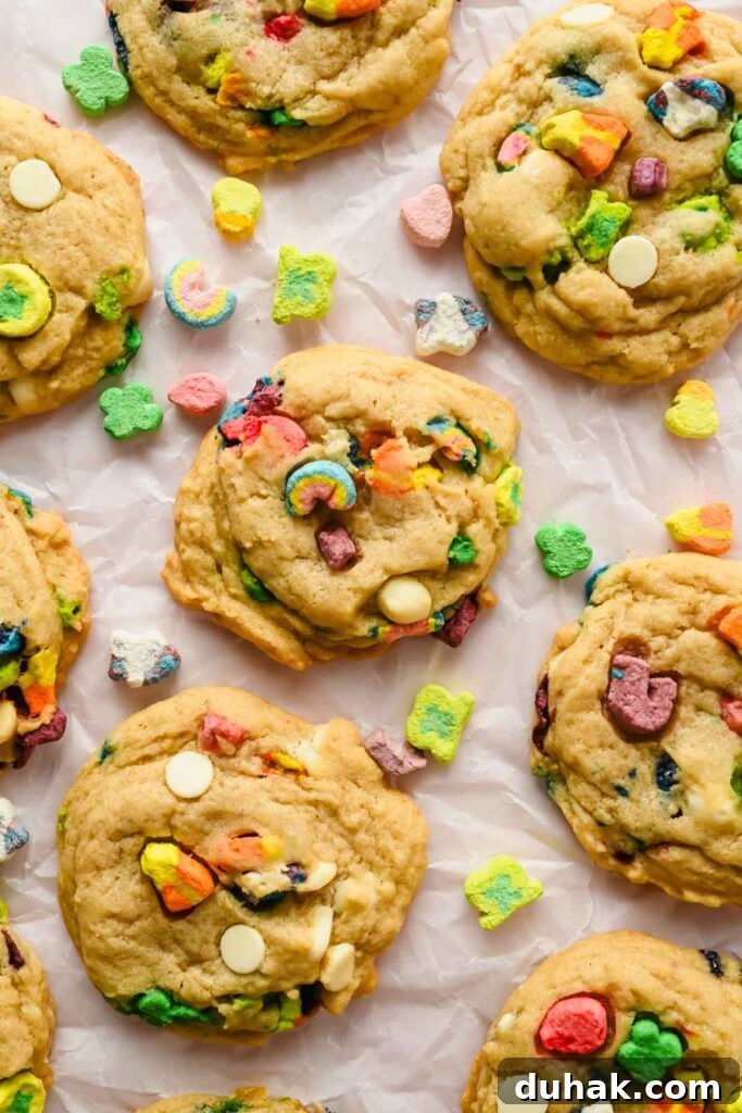 baked lucky charm sugar cookies on parchment paper with additional lucky charm marshmallows scattered.