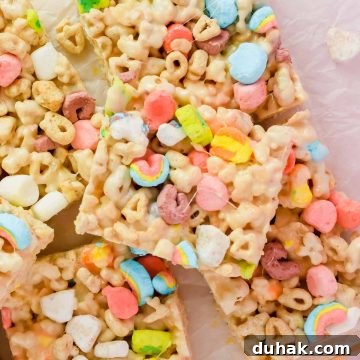 stacked lucky charm rice krispie treats cut into squares on white parchment.