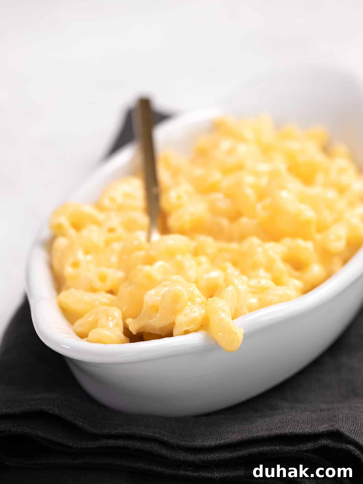 Macaroni and cheese in a white boat with a fork, on a dark gray napkin