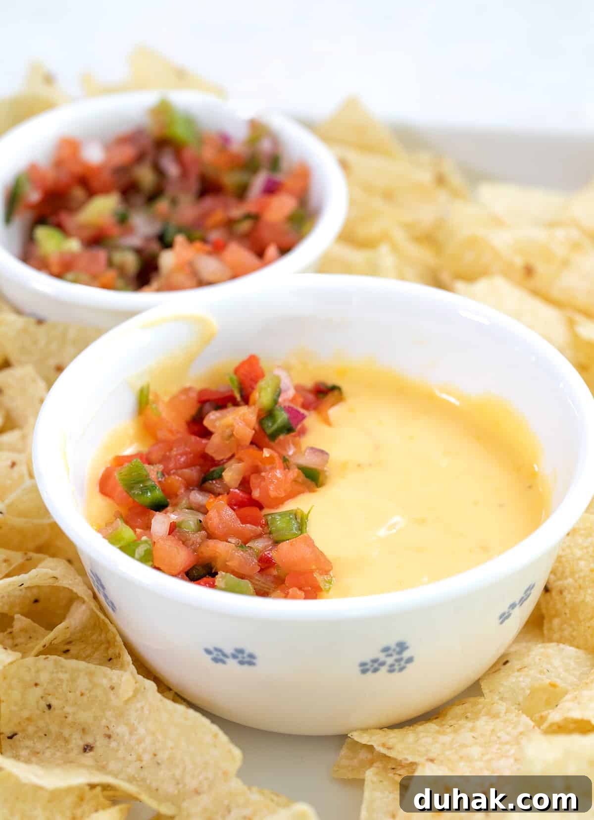 Cheese sauce in white bowl surrounded by chips on white tray