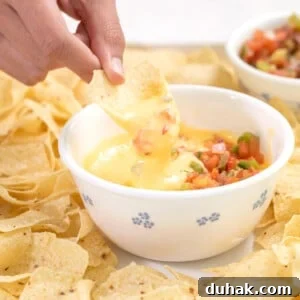 fingers holding tortilla chip and dipping gluten free cheese sauce from small white bowl