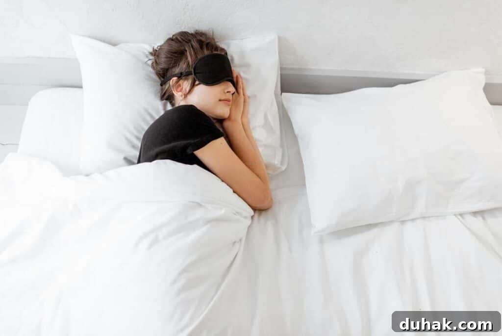 Stop Snacking: Dietitian-Backed Strategies to Curb Cravings 5 A woman with a sleep mask on sleeping in her bed with white blankets and pillows.