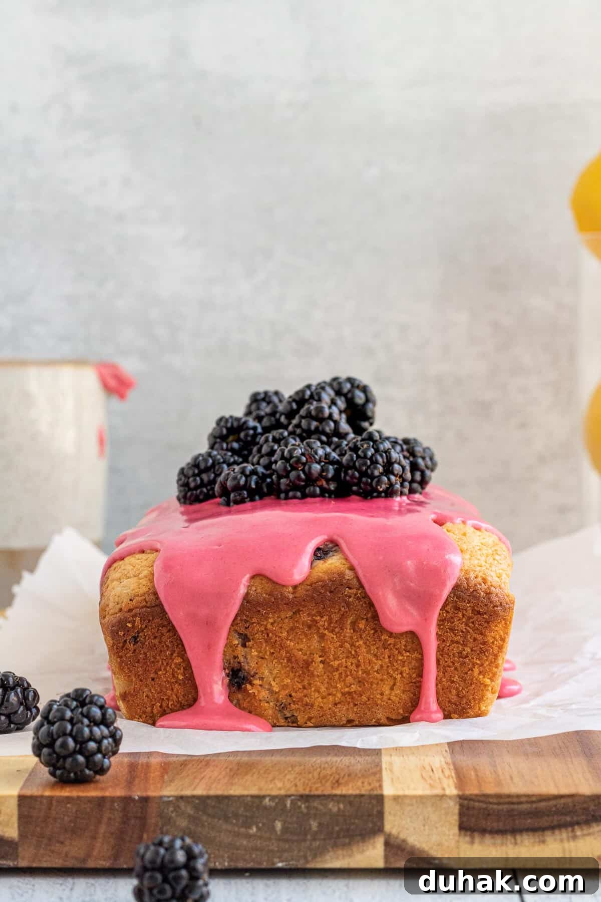 Lemon Blackberry Quick Bread Recipe for Moist Loaves 5 blackberry lemon bread with a pink glaze and blackberries on top sitting on a parchment covered wood board