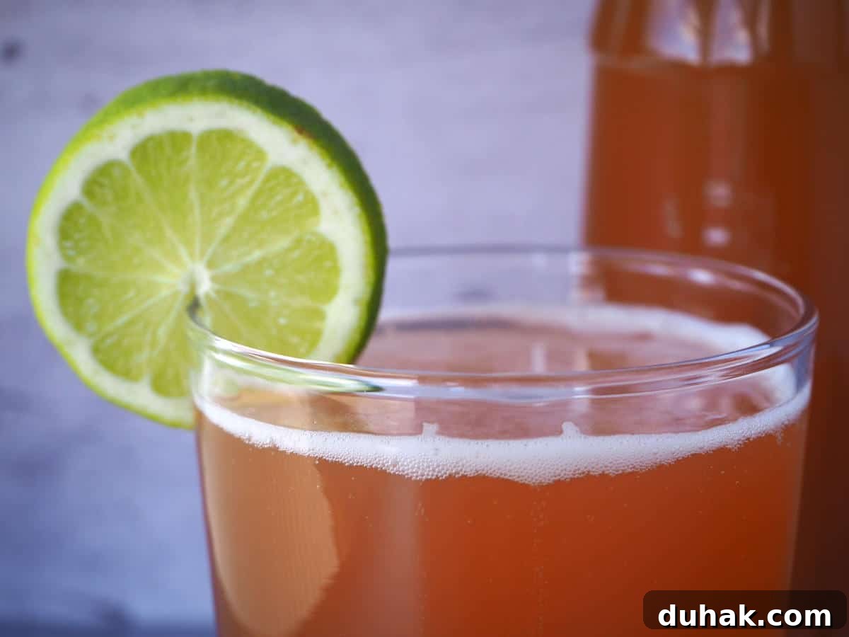 How to Make Homemade Cola Soda from Scratch 18 close up of glass of homemade cola with lime circle garnish and bottle of cola in background.