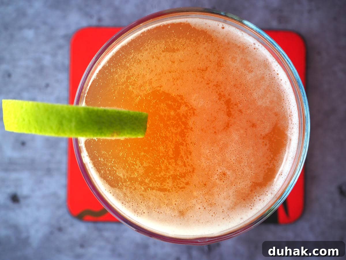 How to Make Homemade Cola Soda from Scratch 19 Top down view homemade cola in glass with lime circle garnish on side, with a red coaster under the glass.