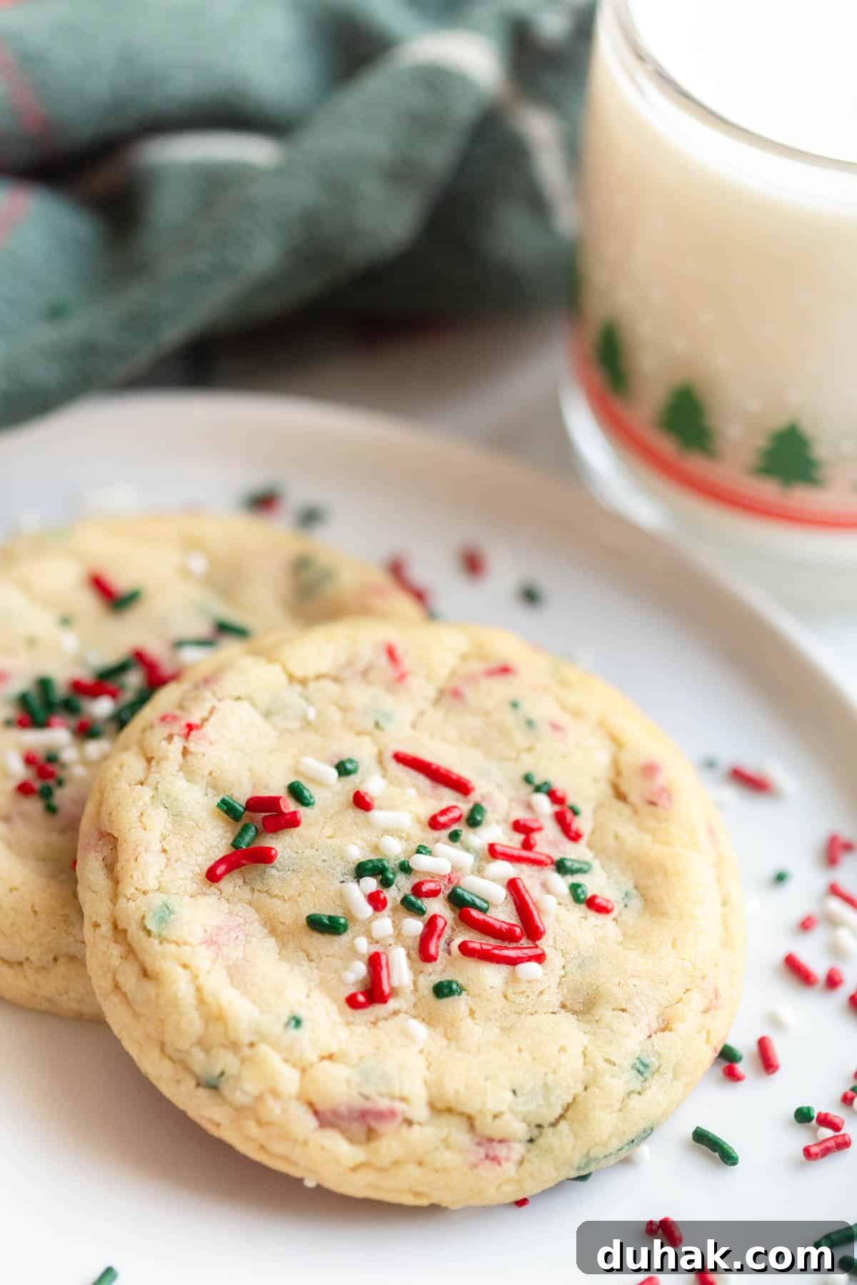 Christmas Sprinkle Sugar Cookies Recipe for Festive Holiday Baking 5 Christmas Sprinkle Sugar Cookies on a white plate with a mug of milk and a festive towel in the background.