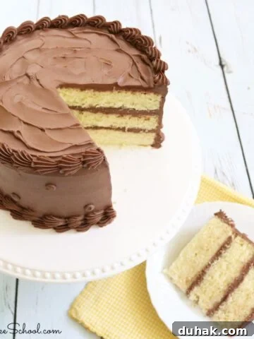 Sliced yellow cake with chocolate frosting on white pedestal with a plated slice next to it.