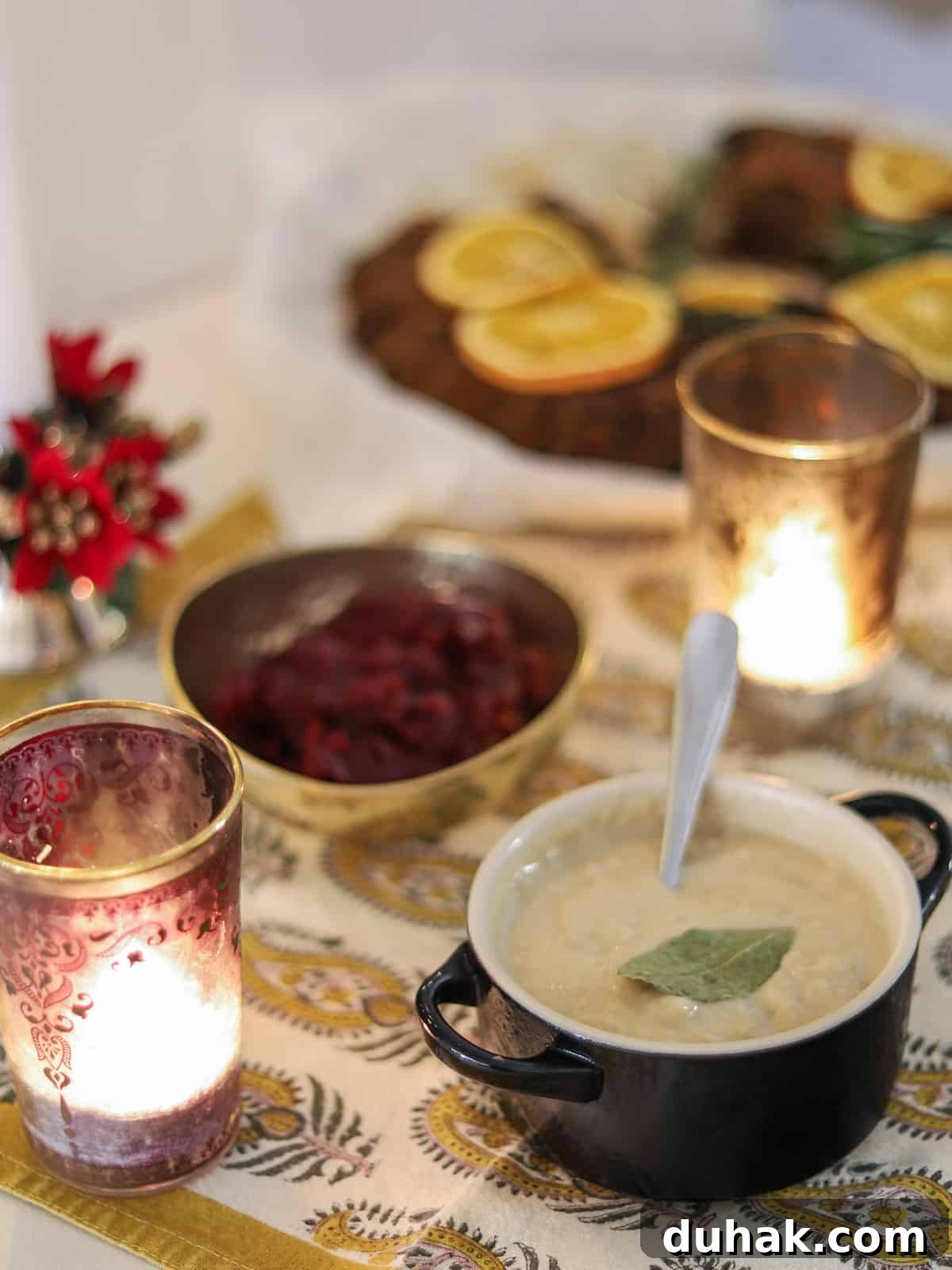 Photo of a dish of bread sauce on a set table with candles and cranberry sauce in the background and a nut roast at the back.