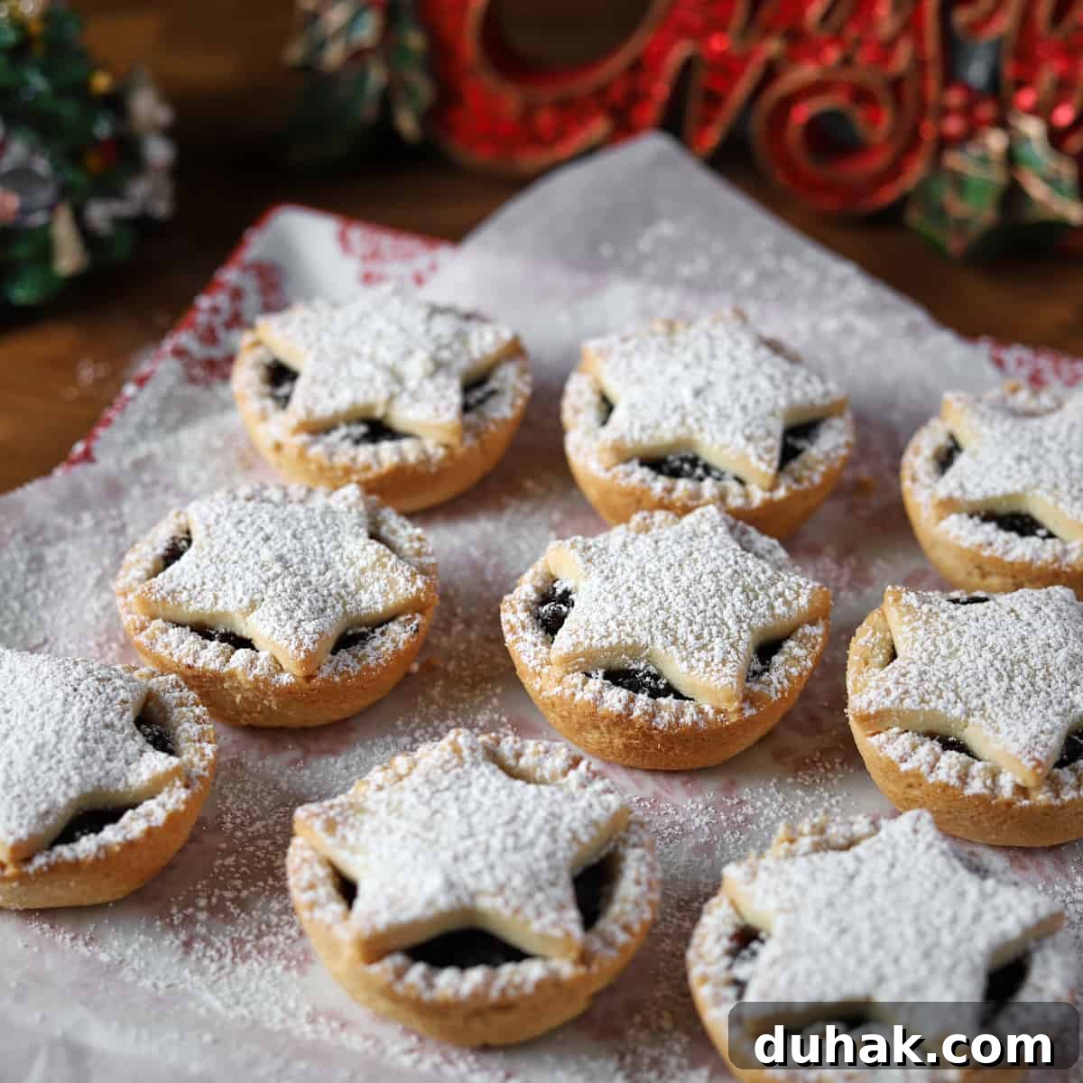 Square photo of 9 star-topped, icing sugar dusted vg gf mince pies with christmas ornaments in the background.