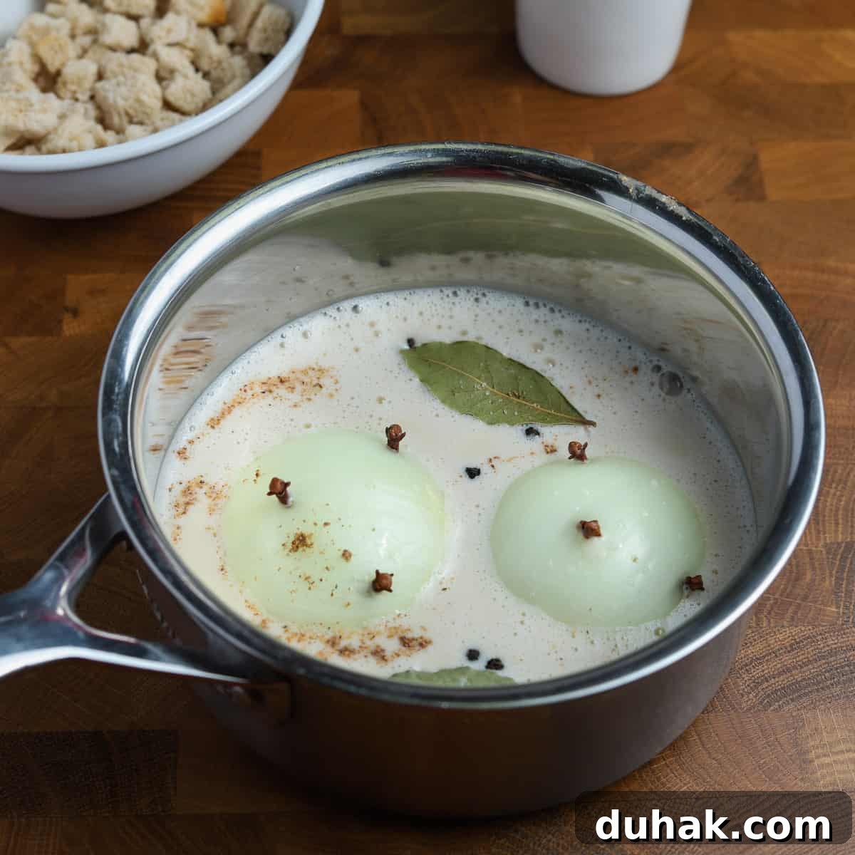 Photo of a pan containing oat milk, clove studded onions, bay leaf, and spices.