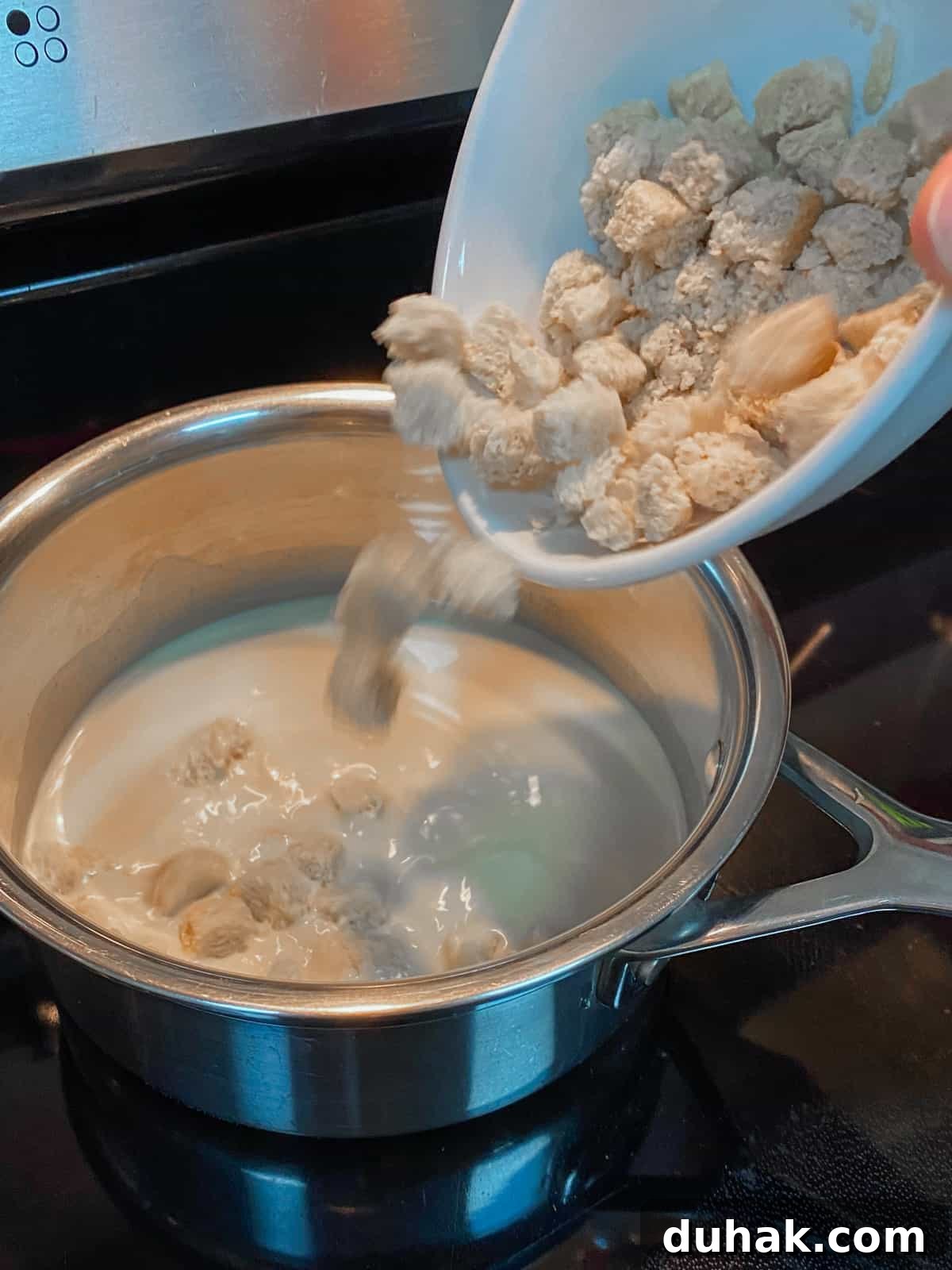 Photo of milk in the pan and adding GF bread cubes to the pan.