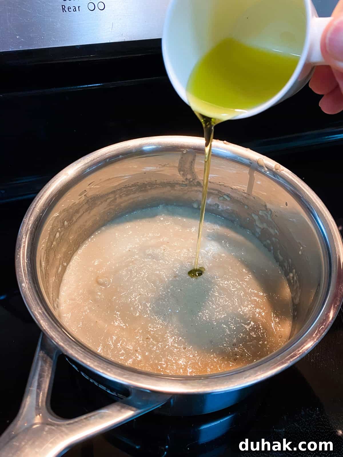 Photo of a pan of bread sauce and pouring oil in to enrich at the end.