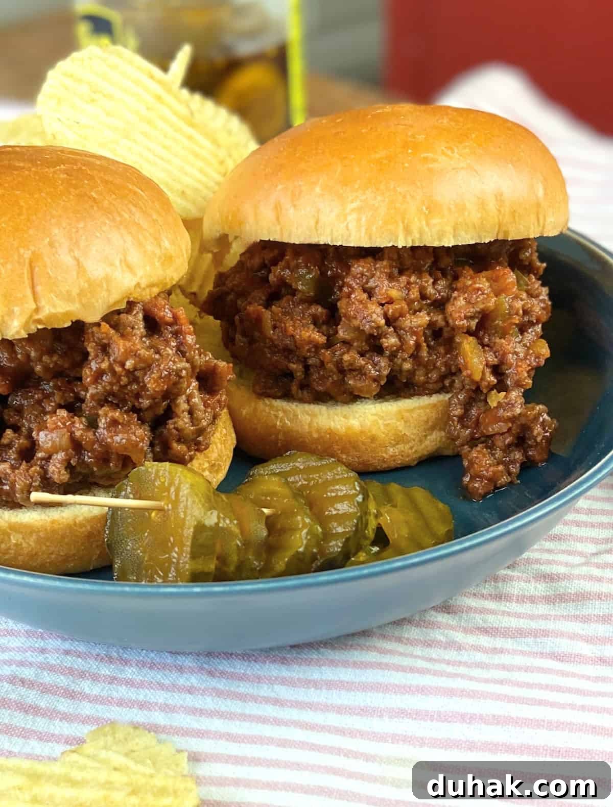 Classic Homemade Sloppy Joes Recipe for Perfect Weeknight Dinners 2 Two sloppy joe's sandwiches on blue plate with chips and pickles.