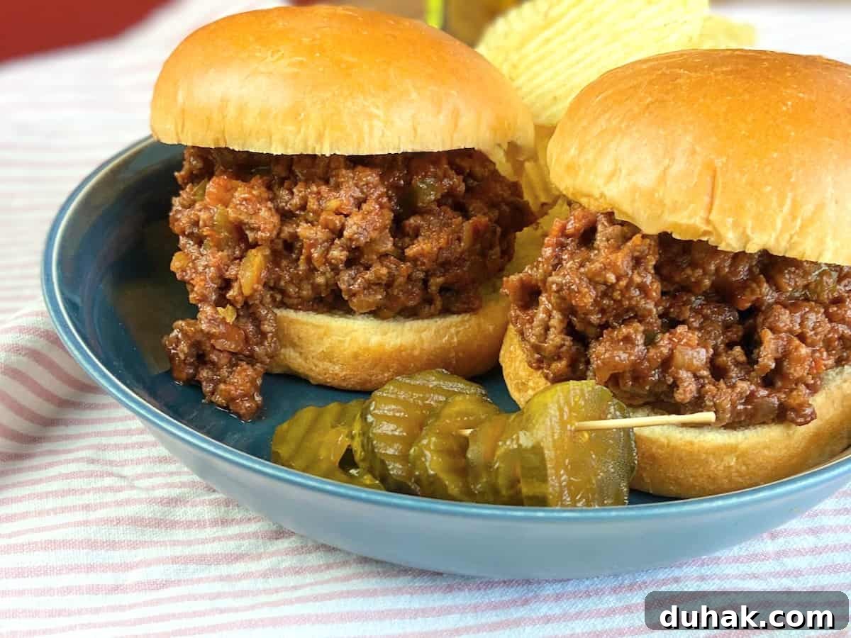 Classic Homemade Sloppy Joes Recipe for Perfect Weeknight Dinners 4 Two sloppy joe's on a blue plate with chips and pickles.