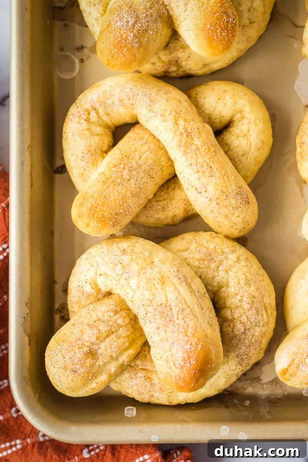 Overhead shot of soft pretzels arranged on a baking sheet with an orange towel on the side.