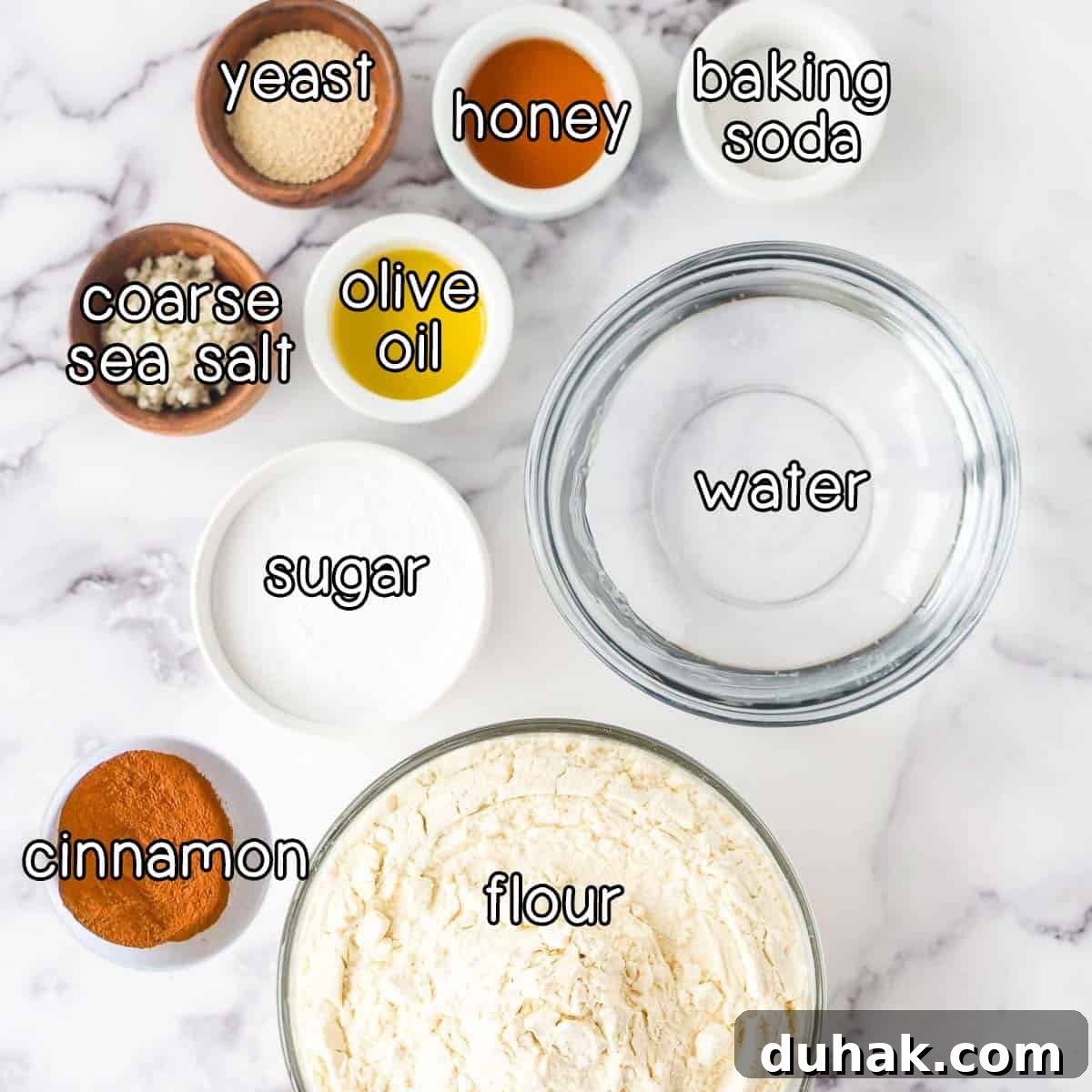 Overhead shot of ingredients - yeast, honey, baking soda, coarse sea salt, olive oil, sugar, water, cinnamon, and flour.