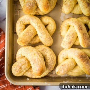 Overhead shot of soft pretzels arranged on a baking sheet with an orange towel on the side.