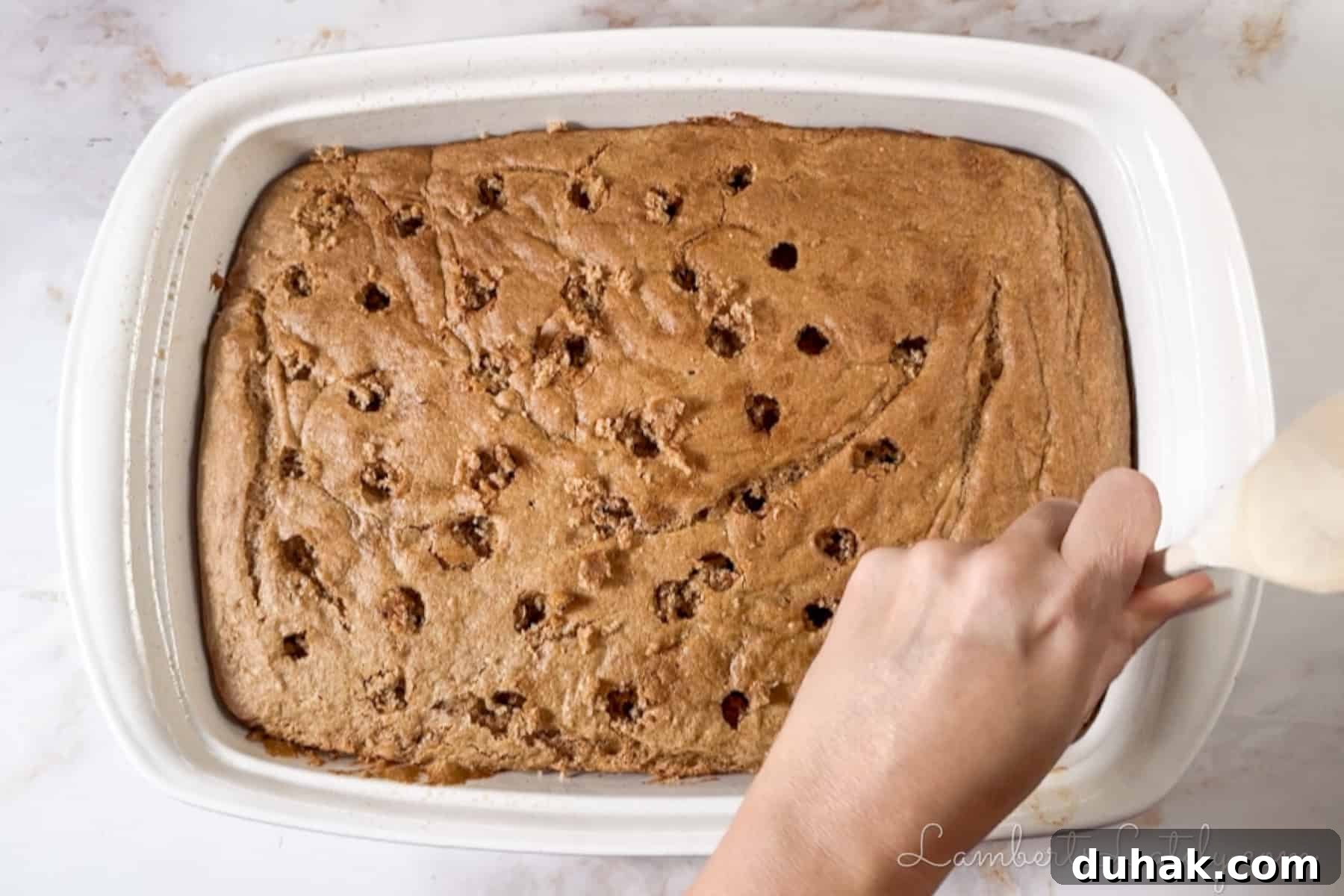 Creamy Eggnog Poke Cake Recipe for Holiday Dessert 5 poking holes in a baked spice cake with the back of a wooden spoon.