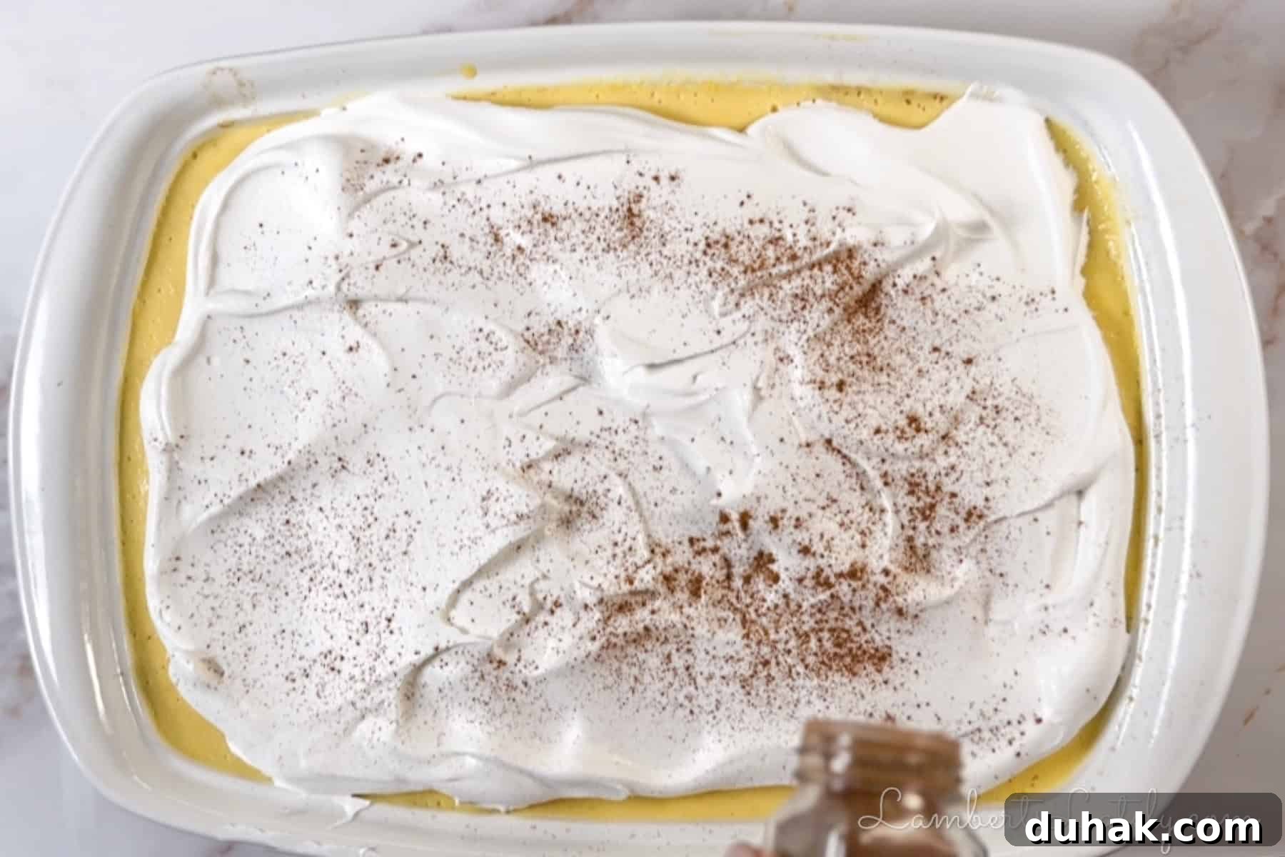 Creamy Eggnog Poke Cake Recipe for Holiday Dessert 7 sprinkling cinnamon on top of the finished cake.