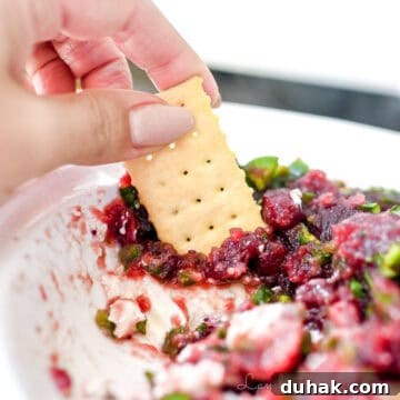 dipping a cracker into cranberry jalapeno dip.