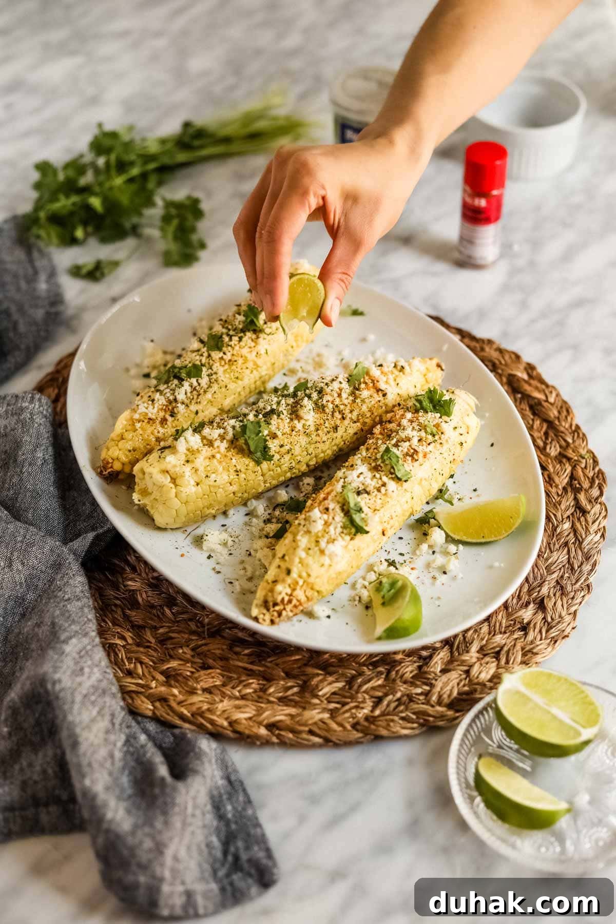 Hand squeezing lime juice on elote-style corn with furikake and kewpie mayo.