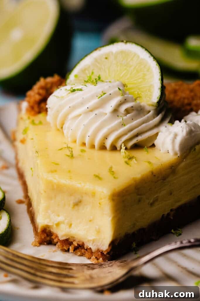 A close-up of a slice of key lime pie on a plate, with a bite missing to reveal the ultra creamy texture.