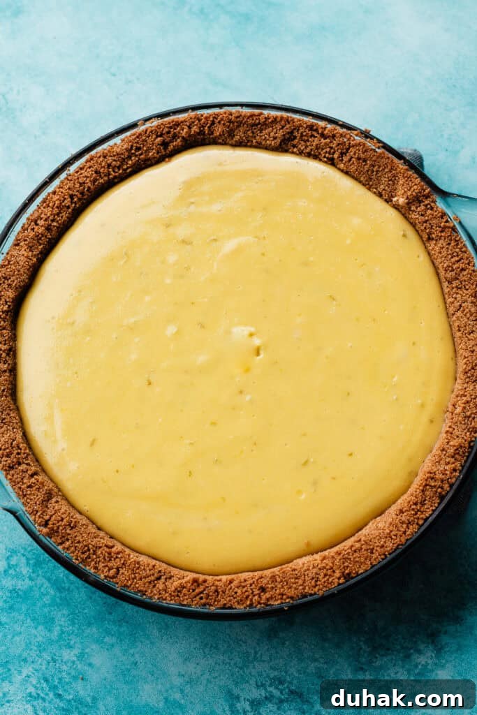 The baked key lime pie resting on a blue surface. The pie has a slightly raised look on the surface that will disappear as it cools.