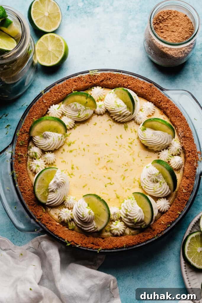 The baked, chilled pie on a blue surface, decorated with swirls of whipped cream and lime slices.