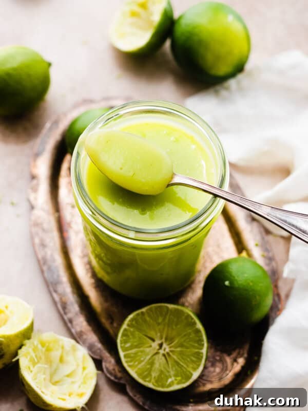 A spoon resting on a jar of bright green lime curd.