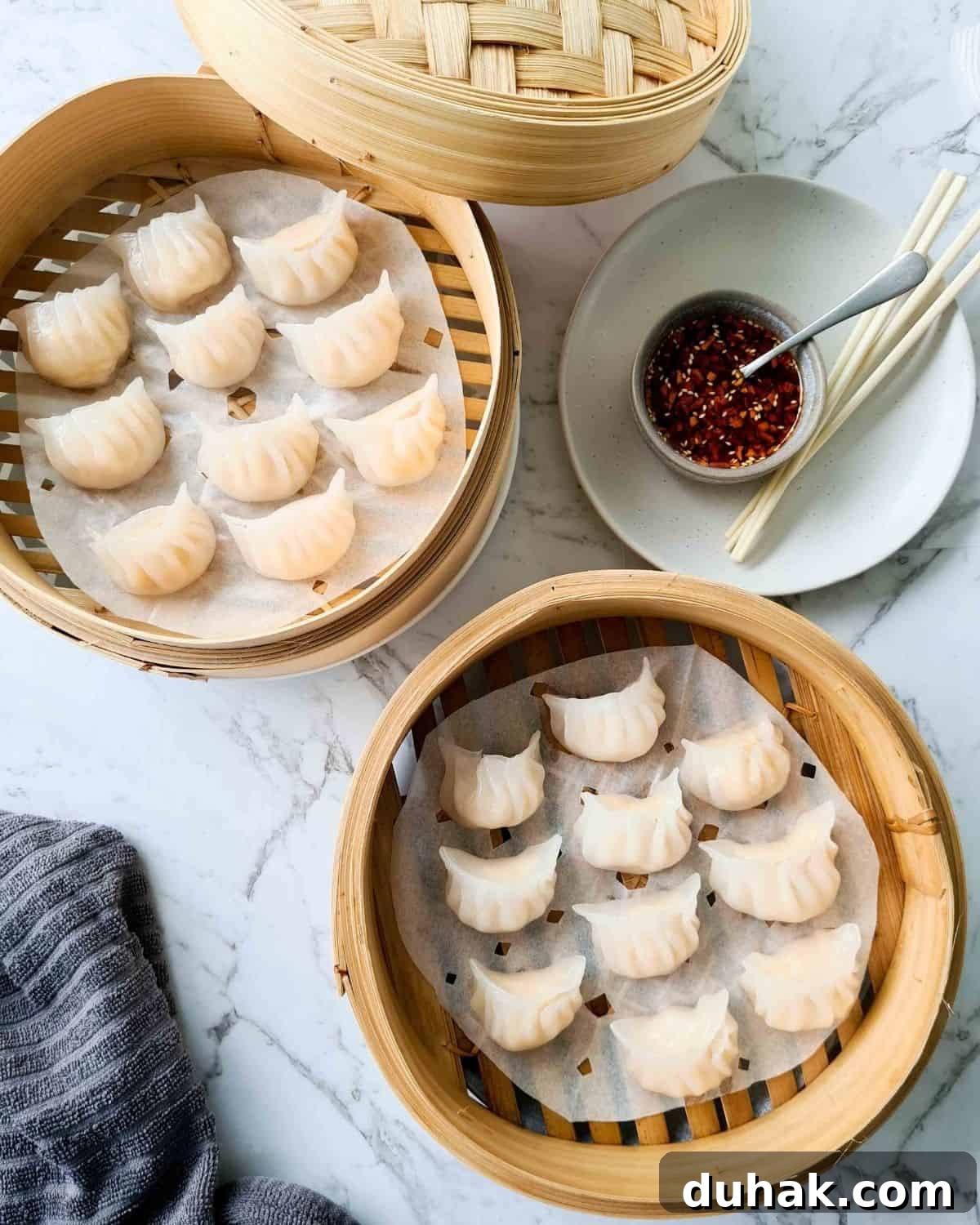 Two baskets filled with cooked dumplings with a side of dipping sauce