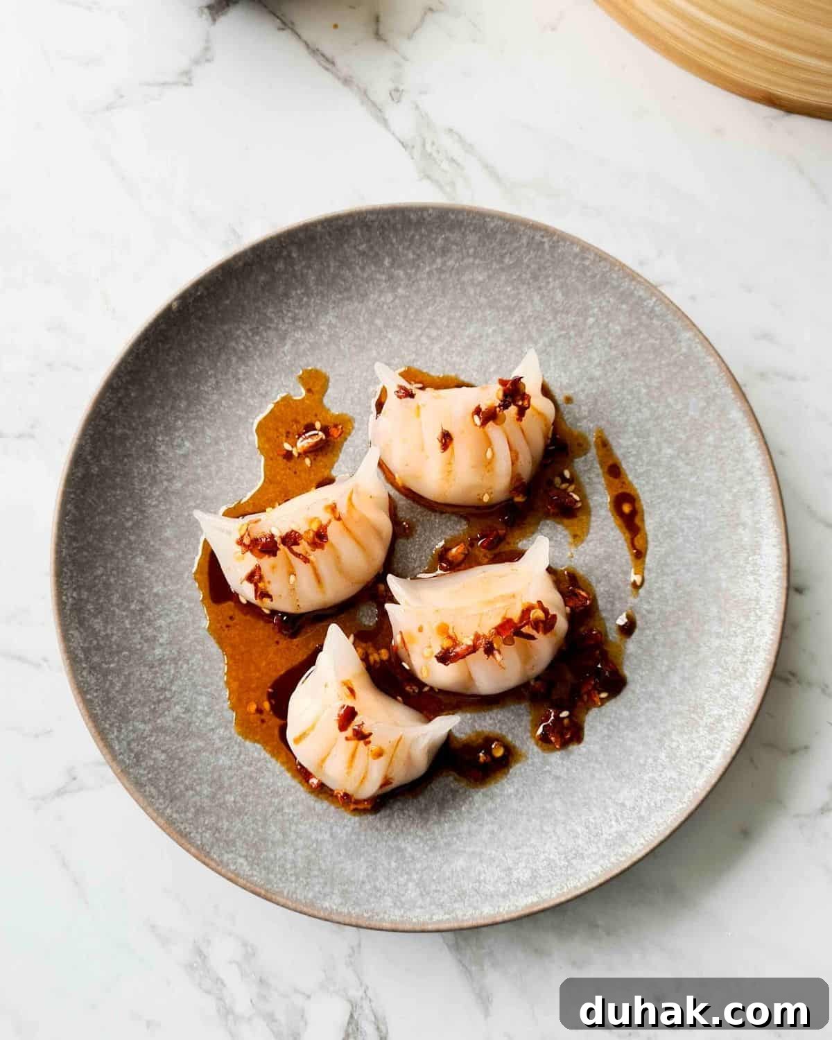 Close up plate of 4 cooked har gow drizzled with dipping sauce