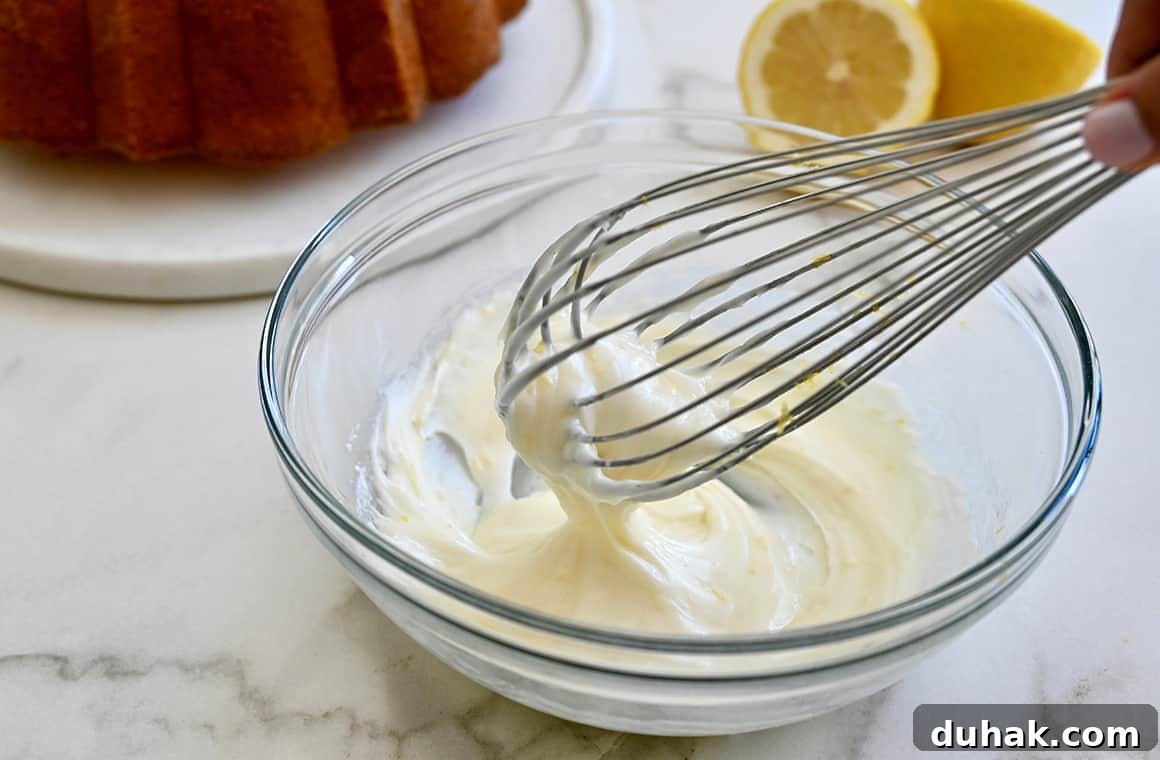 Glazed Lemon Pound Cake Recipe with Zesty Drizzle 6 A clear bowl with icing and a wire whisk