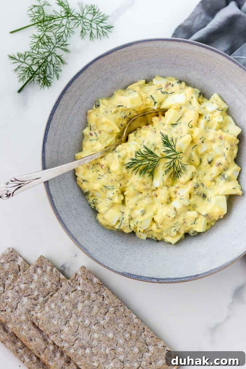 Creamy Egg Salad with Dill, Capers & Lemon Zest 2 Egg salad in a bowl with a spoon next to crackers and dill sprigs.