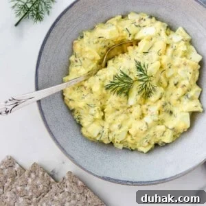 Creamy Egg Salad with Dill, Capers & Lemon Zest 14 Egg salad in a bowl with a spoon next to crackers and dill sprigs.