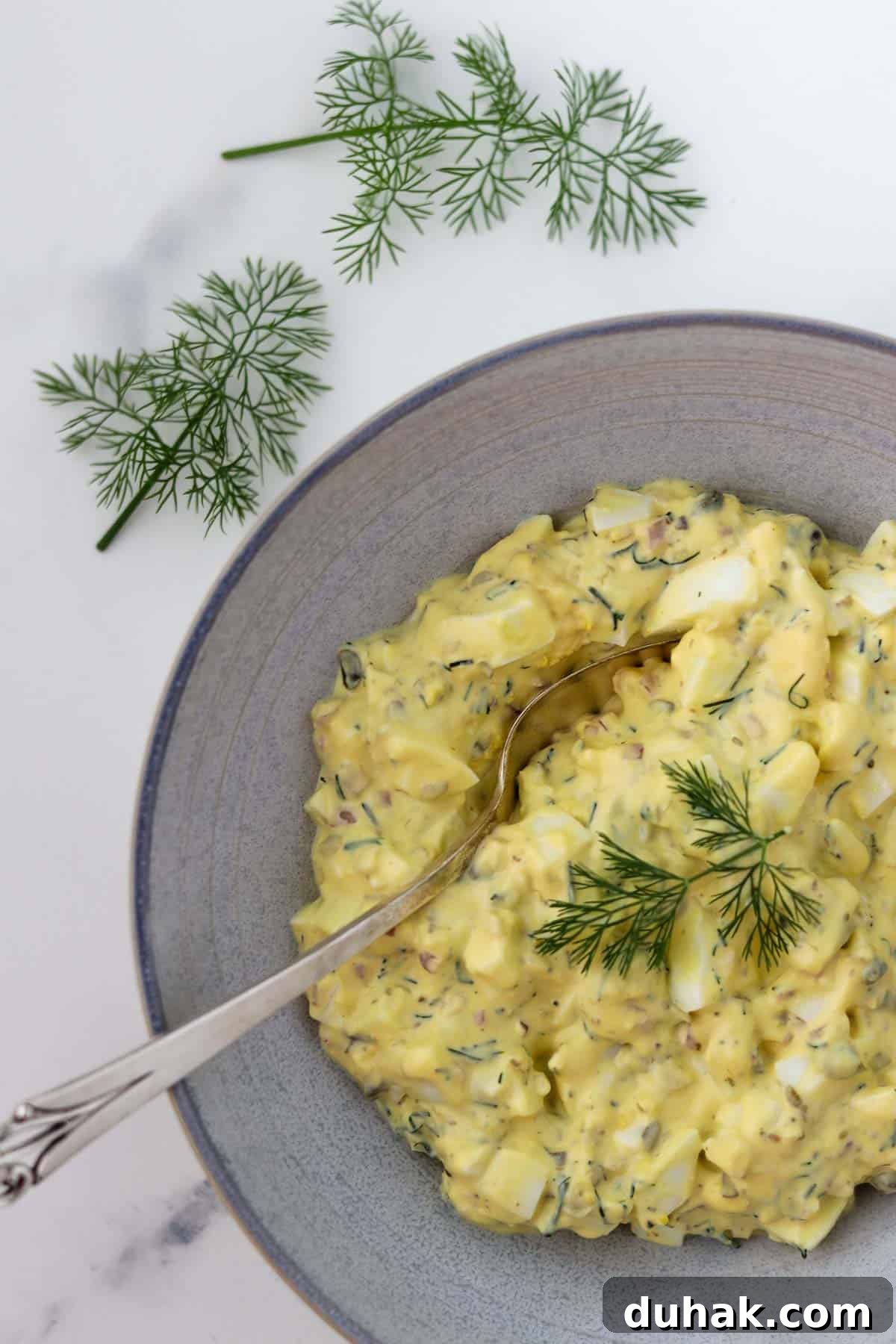 Creamy Egg Salad with Dill, Capers & Lemon Zest 8 Egg Salad in a bowl with a spoon next to dill sprigs.