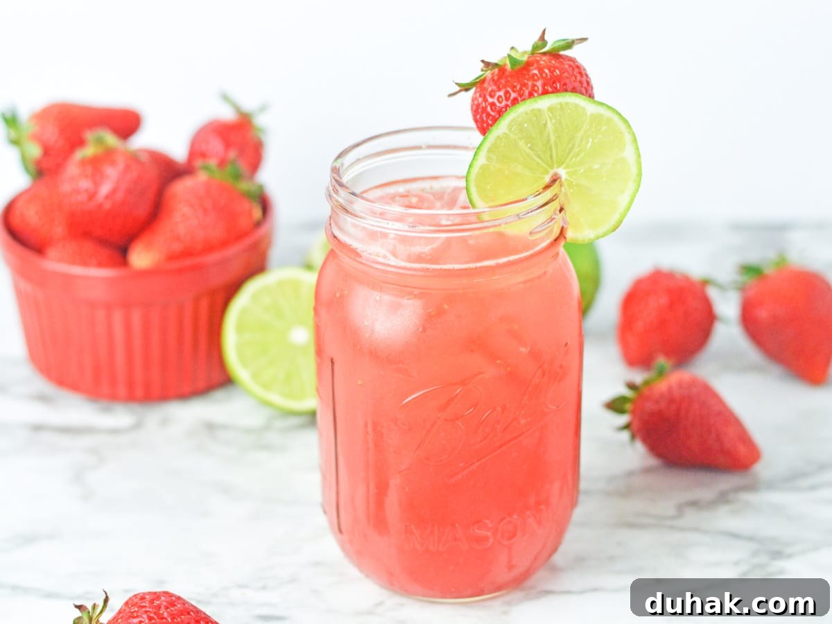 strawberry agua fresca in a mason jar glass with ice and scattered fruit in the background
