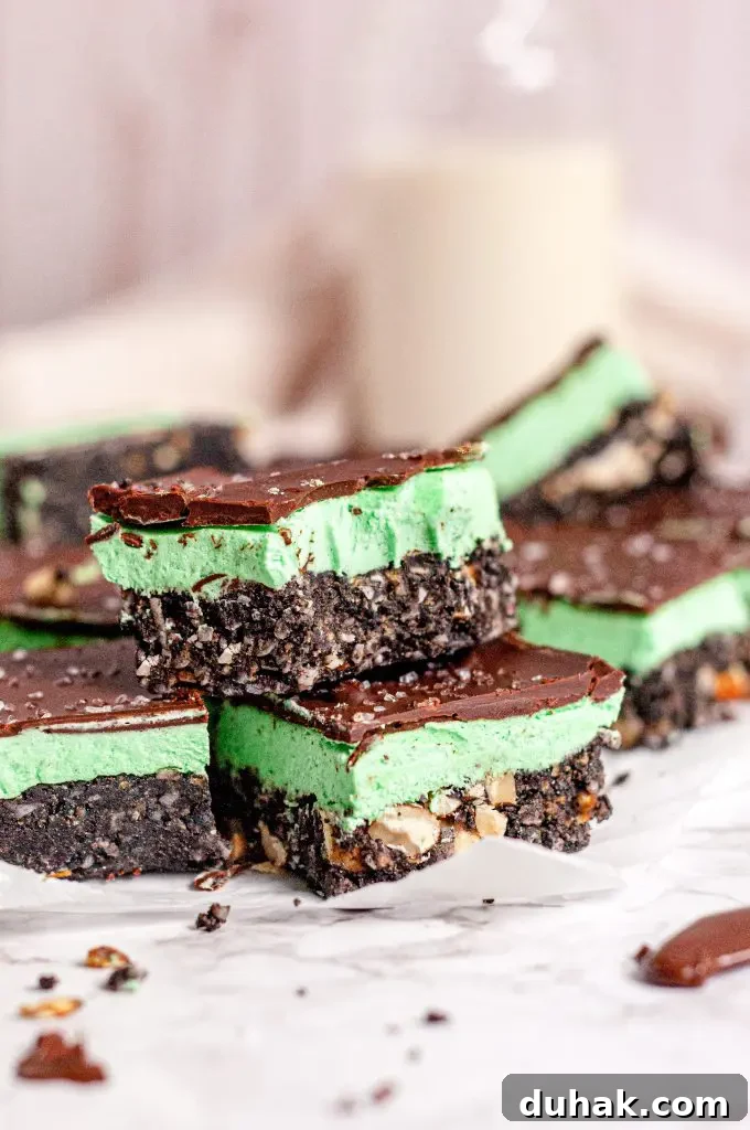 Vegan Gluten-Free Christmas Cookie Recipes 15 A bunch of cut up mint green and chocolate Nanaimo bars on a table. The front two nanaimo bars are stacked and the top one has a bite out of it.