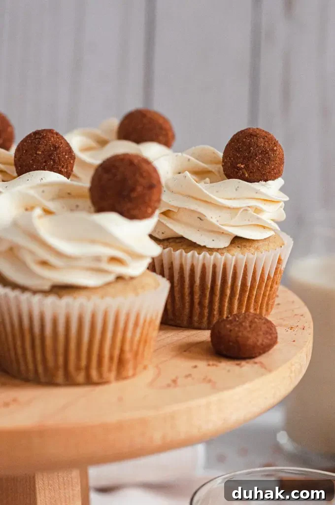 Vegan Gluten-Free Christmas Cookie Recipes 16 Eggnog cupcakes sitting on a wooden cake stand. They are topped with a white frosting swirl and a mini snickerdoodle cookie for decor.