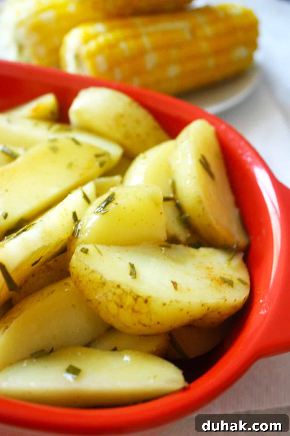 A red bowl of cooked oven roasted rosemary potatoes covered in butter and rosemary.