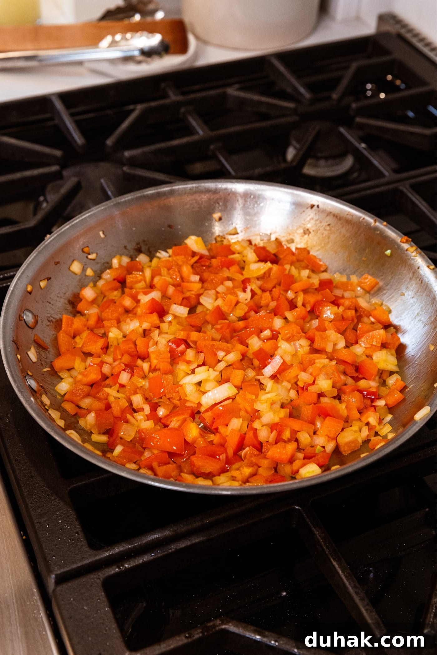 Cheesy Turkey & Spaghetti Squash Casserole Recipe 12 Metal skillet on stovetop filled with diced red bell pepper and onion over hot heat.