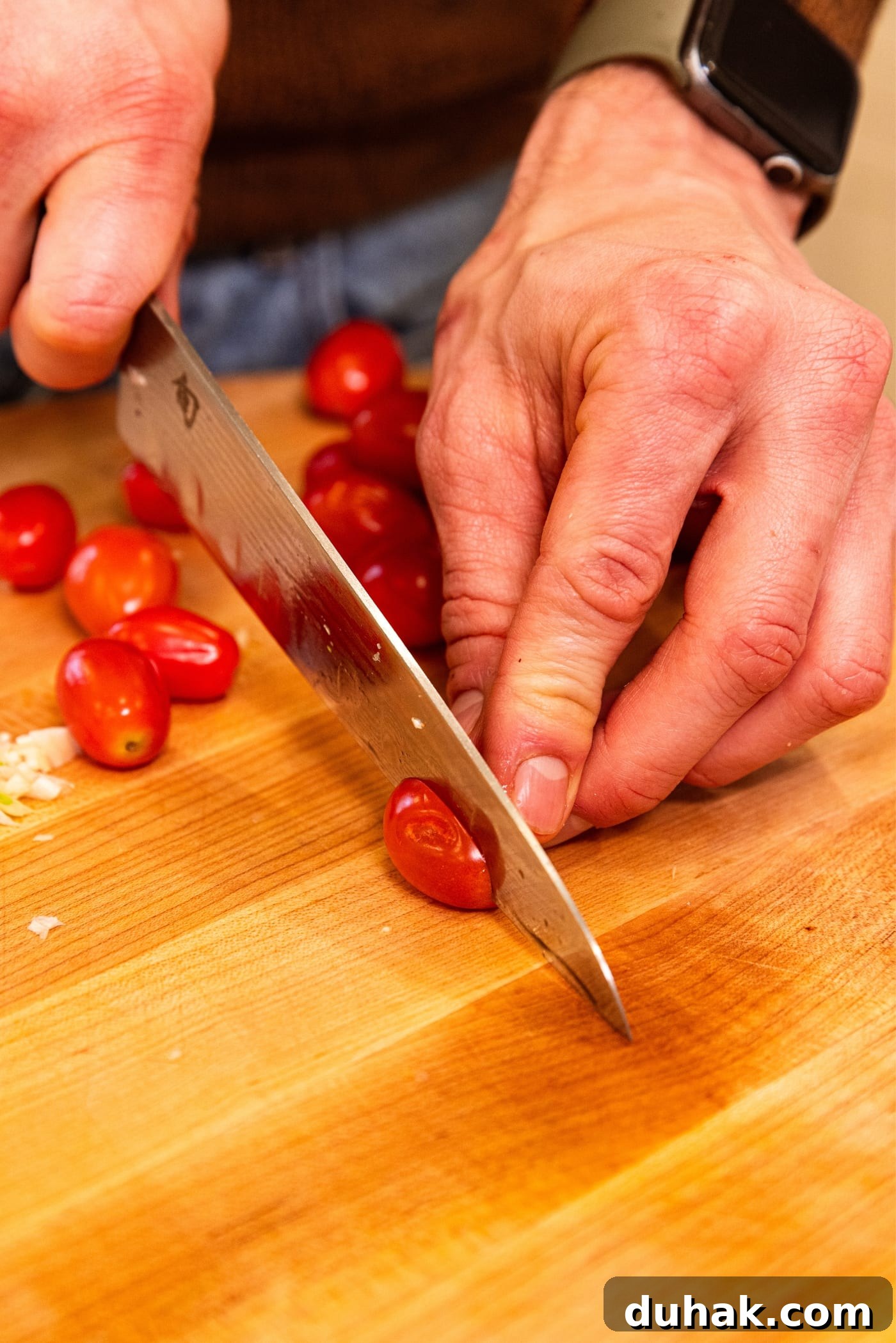 Cheesy Turkey & Spaghetti Squash Casserole Recipe 13 Hand using knife to slice cherry tomatoes in half on wooden cutting board.
