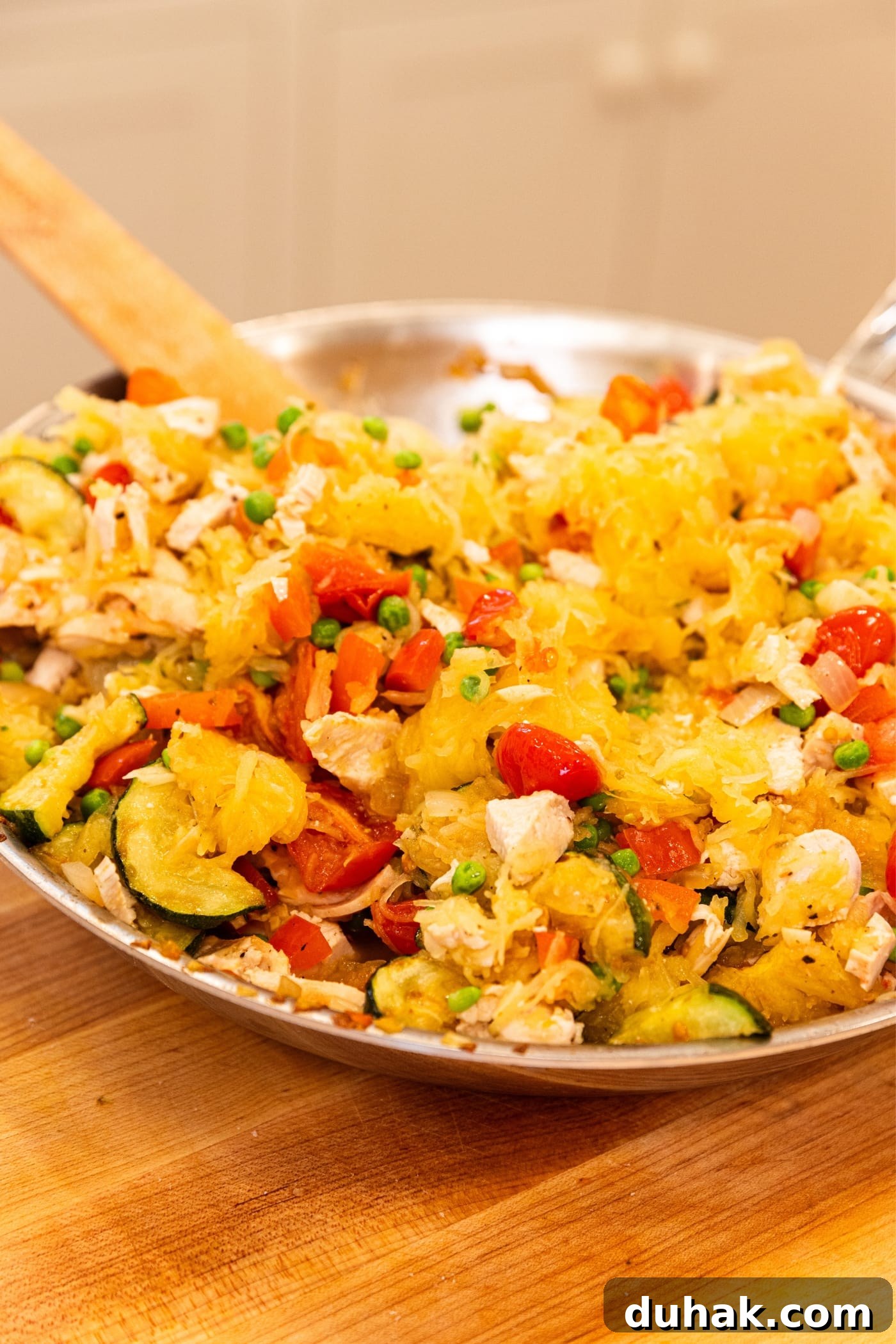 Cheesy Turkey & Spaghetti Squash Casserole Recipe 18 Metal skillet sitting on wooden cutting board filled with zucchini, tomatoes, chicken, and yellow-colored spaghetti squash after being mixed together.